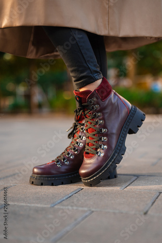 Foto person wearing burgundy boots standing on urban pavement in casual outdoor setting close-up of feet and lower legs with leather and velvet materials and green grass background