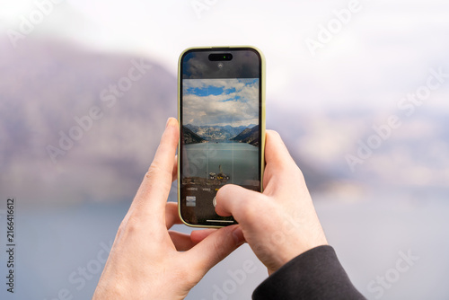 Foto Close-up view of a person holding a smartphone and capturing a stunning view of a scenic bay surrounded by mountains