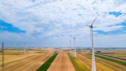 Foto Wind turbines stand tall in fields under a blue sky with clouds