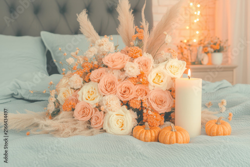 Luxurious autumn floral arrangement with peach roses pampas grass small pumpkins and glowing pillar candle.