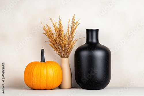 Cozy autumn still life with bright orange pumpkin black ceramic bottle vase and dried flowers on white background.