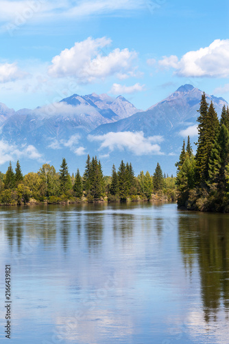 Beautiful summer landscape of calm Irkut River and the Eastern Sayan Mountains under light morning clouds in August. Natural background. Siberia, Buryatia, Baikal region, Tunka Valley, Nature Park