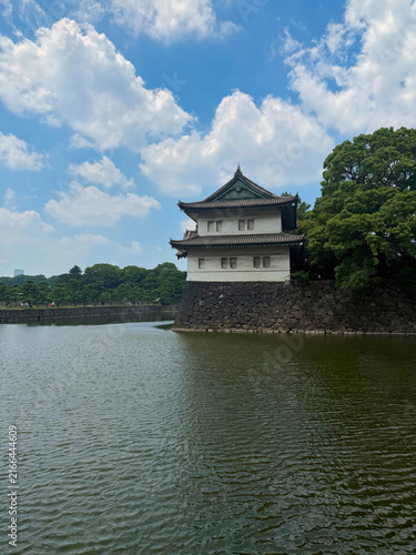 Sakurada-Niju-Yagura Watchtower at the Imperial Palace in Tokyo, Japan, standing above a stone wall beside the moat, surrounded by lush trees under a blue summer sky