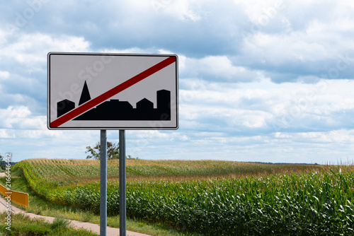 Road sign marking the end of a built-up area beside a rural road, corn field and bicycle path in a sunny countryside landscape