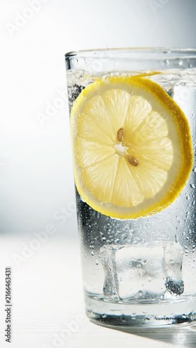 Water being poured into a glass with a fresh lemon slice and ice cubes for a refreshing drink
