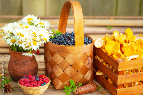 Ripe juicy blueberries in a wicker basket, raspberries, chanterelles in a wooden crate  and chamomile flowers.