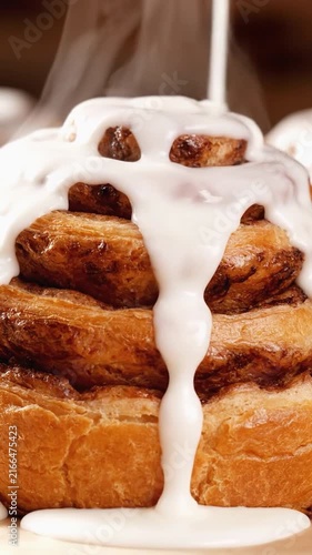 White icing dripping down a freshly baked cinnamon roll with steam rising in a cozy bakery