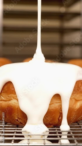 White liquid sugar glaze being poured over a fresh ring donut on a wire rack in a bakery