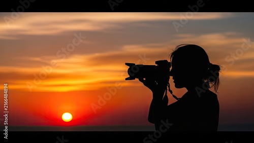 Silhouette of female photographer taking pictures at sunset.