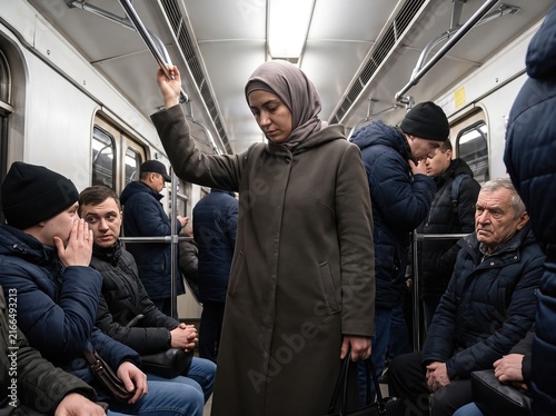 Woman in Hijab standing on train while passengers cast suspicious unfriendly glances