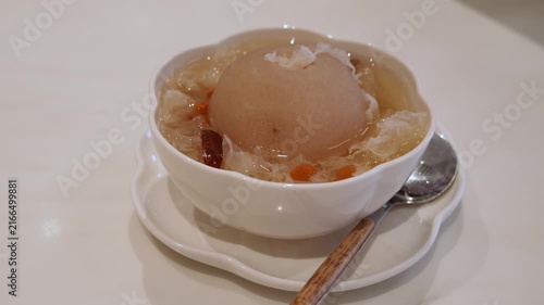 Traditional Chinese sweet dessert soup featuring a whole pear surrounded by snow fungus, dried red dates, and goji berries in a light sweet broth.