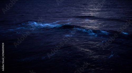 Bioluminescent ocean waves at night, glowing blue plankton in dark sea water, neon light effect on crashing surf
