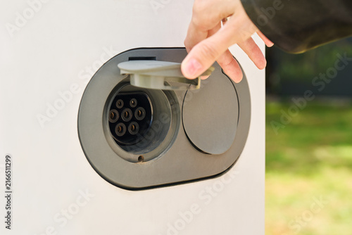 Foto A close-up of an electric vehicle's charging port with the protective cover open and a hand preparing the connector for charging