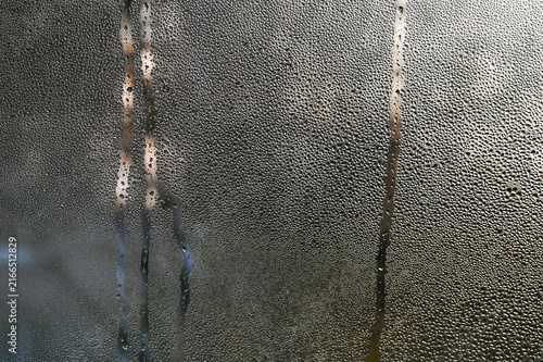 Condensation with water droplets and long streaks on wet glass, condensation creating abstract background. Moist surface shows humidity, cooling air, night reflections, calm atmospheric texture.