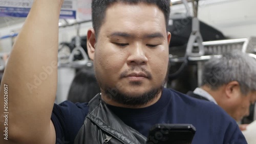 asian man using mobile phone while riding on train commuter subway train texting messaging chatting online or surfing internet, asian man use mobile phone on Tokyo Subway train commuter