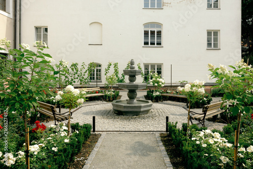 Stone fountain surrounded by blooming white roses in a quiet courtyard garden, lithuania travel content, wedding venue scouting, romantic garden marketing, boutique hotel courtyard promotion