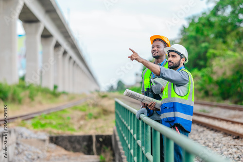 Rail engineer and technician in safety vests discussing track upgrade plan on railway line