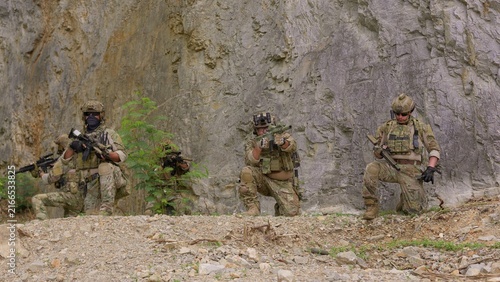 Canvastavla A special forces team conducts a military operation, with soldiers aiming rifles from defensive positions against a rugged rock face background