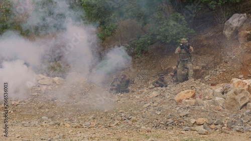 Konstfotografi A tactical squad of soldiers in camouflage advances through rocky terrain under the cover of smoke during a high-stakes military training mission or combat operation