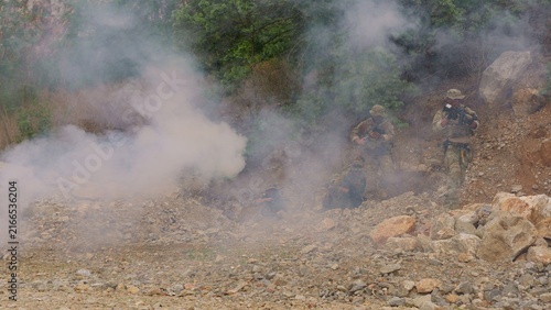 Foto A tactical squad of soldiers in camouflage advances through rocky terrain under the cover of smoke during a high-stakes military training mission or combat operation
