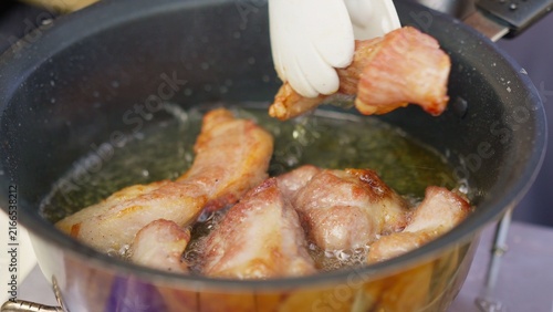Quadro su tela A chef using tongs carefully places pieces of pork into a pan of hot bubbling oil, deep-frying the meat until it becomes golden brown and deliciously crispy for a meal