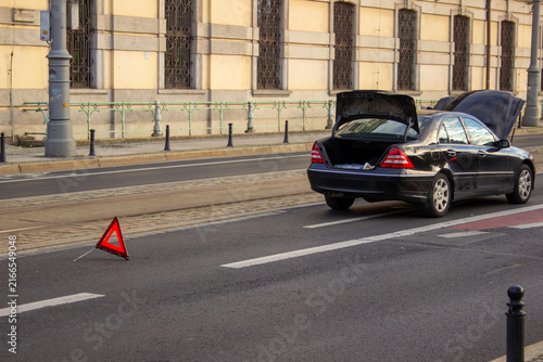 фотографія Black sedan with open trunk and hood parked on a city street beside a warning triangle, apparent breakdown scene