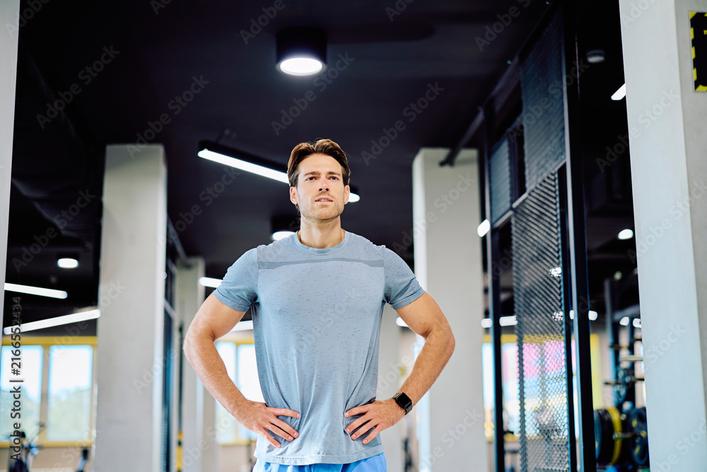 Naklejka premium Athletic man standing with hands on hips, looking focused and determined during a workout session at a contemporary gym