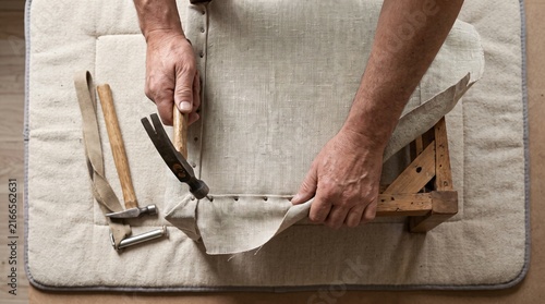 Hands Stretching New Fabric Over A Chair Seat Frame as a Furniture Restoration Metaphor