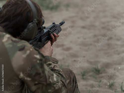 Canvas Print Over the shoulder view of a soldier settled behind an SA80 rifle, hands steady on the handguard as he prepares to fire