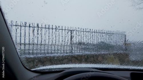Slow motion snow falling beyond a water covered windshield viewed from inside a car