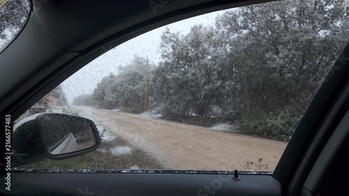 Slow motion snowfall seen through a wet car side window beside a snowy unpaved road and trees