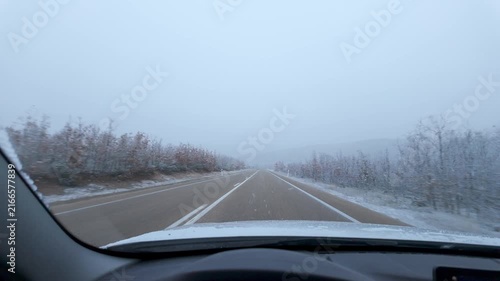 Driving on a snow covered rural highway during active snowfall under an overcast winter sky