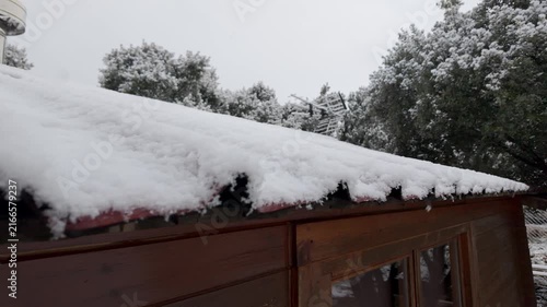 Close view of snow accumulated on a wooden shed roof during cold winter snowfall among trees