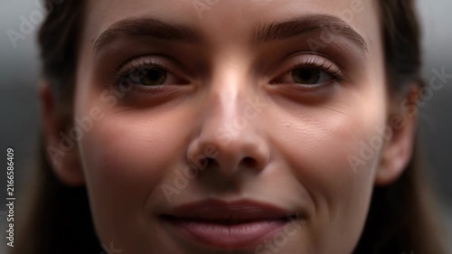 Close-up of a beautiful young woman with closed eyes opening them and smiling gently, serene expression, soft lighting, shallow depth of field