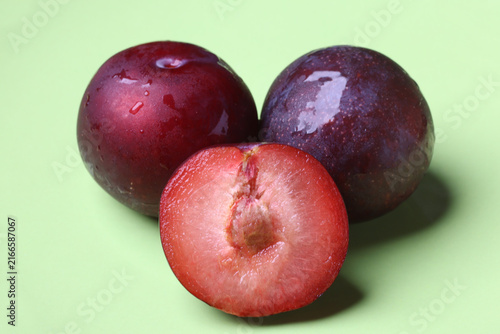 Fresh Red Plums Whole and Half Cut on Green Surface