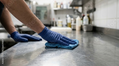 Gloved Hand Wiping Metal Countertop in a Commercial Kitchen