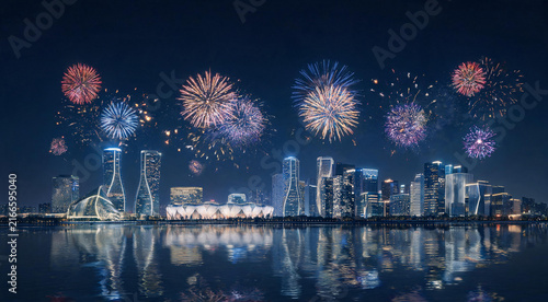 Panoramic city skyline with multiple fireworks displays reflecting on river at night