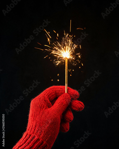 Close-up of hand holding sparkling firework stick with golden light trails
