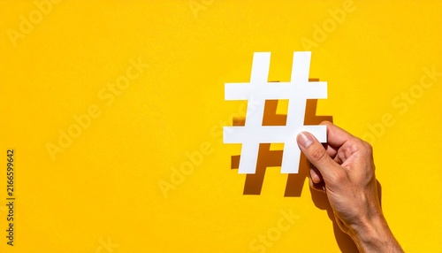 Hand holding a white paper hashtag symbol against a yellow background with social media flat lay cut out communication