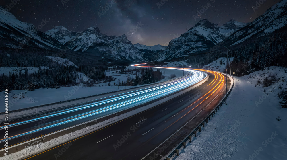 Fototapeta premium Starry night sky over snowy mountain road with vibrant car light trails.