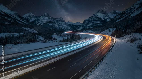Obraz  z motywem Starry night sky over snowy mountain road with vibrant car light trails.