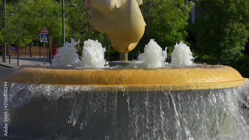 Slow motion water cascading from a yellow sculptural fountain on a sunny city street