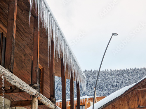 Icicles hang from wooden chalet roof in snowy winter
