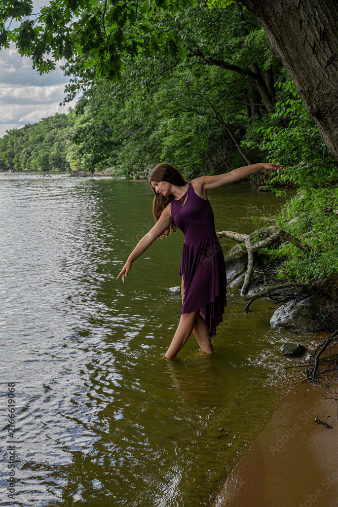 Fototapeta premium Woman Dancing at Lake Shore in Purple Dress Among Trees and Summer Nature