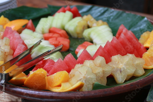 tropical fruit platter features neatly arranged slices of fresh watermelon, starfruit (carambola), melon, papaya, and oranges served over a banana leaf on a traditional platter.