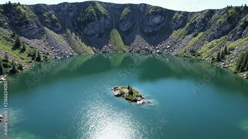 Aerial Drone View of a Pristine Turquoise Crater Lake Surrounded by Rocky Mountains and Pine Trees, with a Small Island in the Center