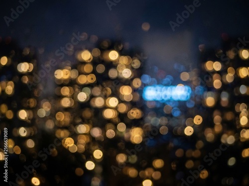 Abstract blurred city lights at night, bokeh effect from rain drops on window glass, urban night scene with warm golden and blue glowing lights