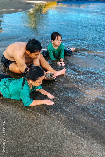 Father and children play together on a sandy beach shoreline, digging and splashing in shallow water. Candid moment of family bonding, summer fun and relaxed outdoor play by the sea.