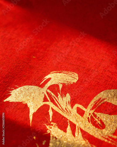 Abstract gold calligraphy brush strokes on textured red paper macro background