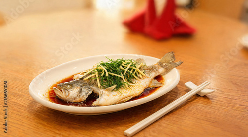 Steamed whole fish with ginger scallion and soy sauce on festive table